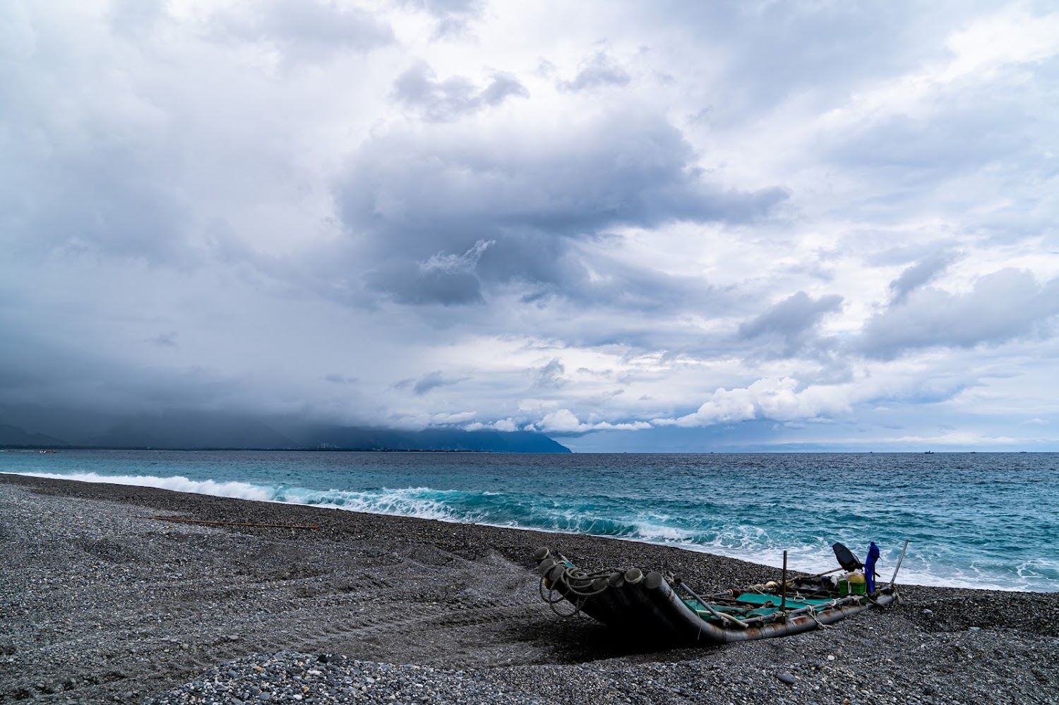 海灘竹筏厚重雲層山脈與拍岸海浪