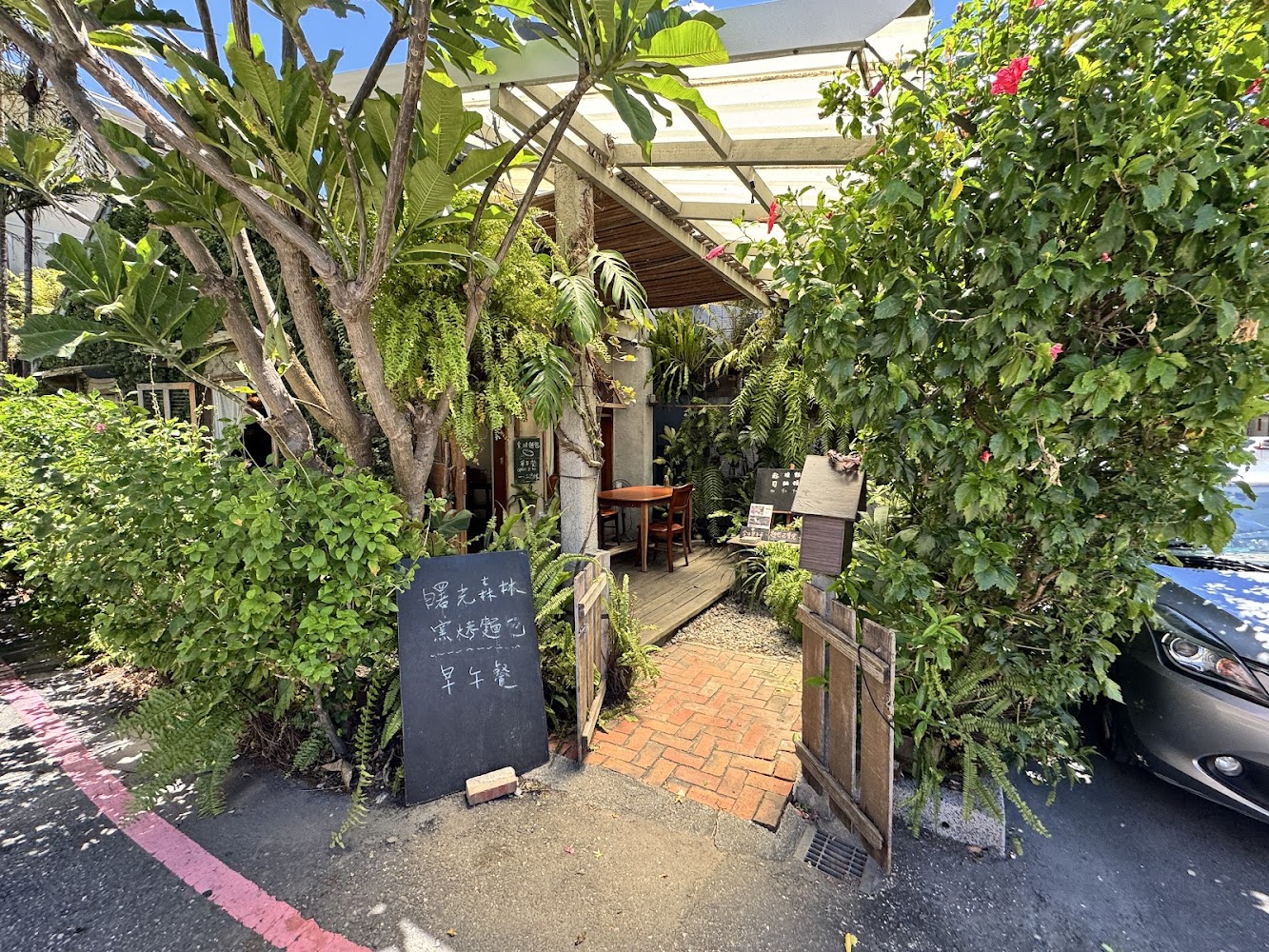 被大量綠意包圍的小店門口，黑板菜單與桌椅充滿悠閒感