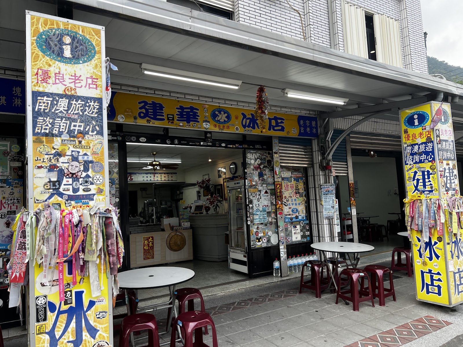 宜蘭南澳建華冰店外觀，黃色廣告柱貼滿旅遊貼紙，南澳旅遊諮詢中心標誌
