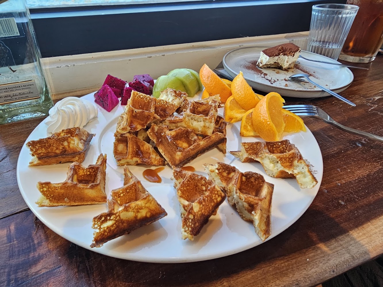 一盤鬆餅搭配水果、提拉米蘇甜點和一杯飲料的豐盛桌面