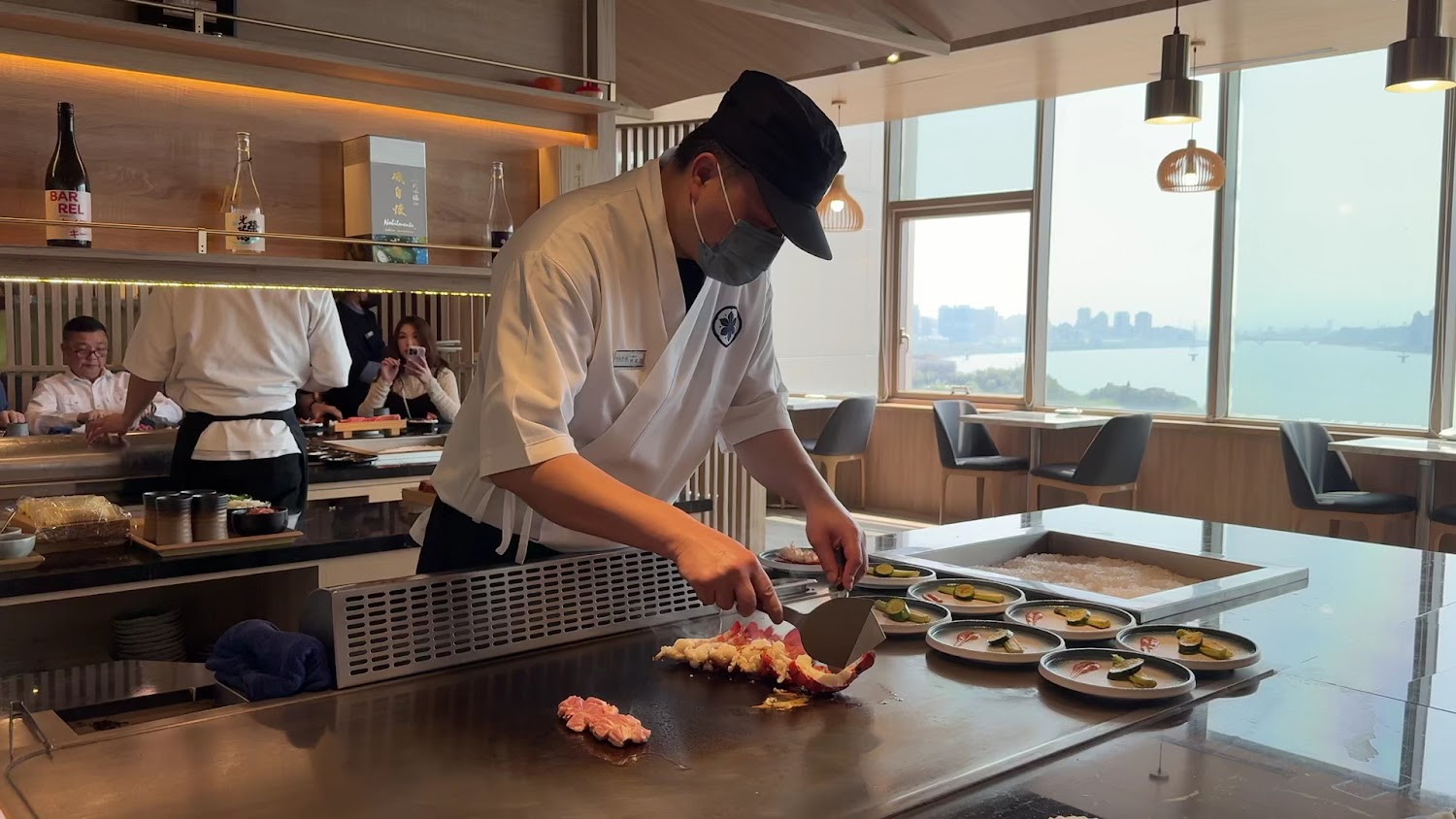 廚師正在鐵板燒餐廳現場料理海鮮，背景可見客人觀賞並拍照