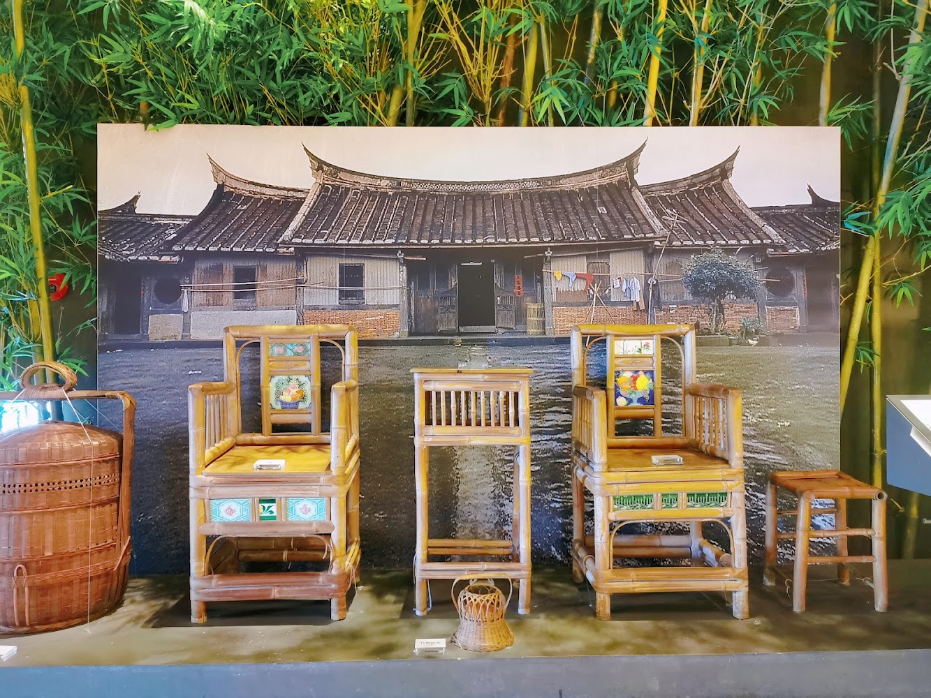 一組傳統竹製家具包含椅子、桌子與提籃，背景是台灣傳統三合院建築
