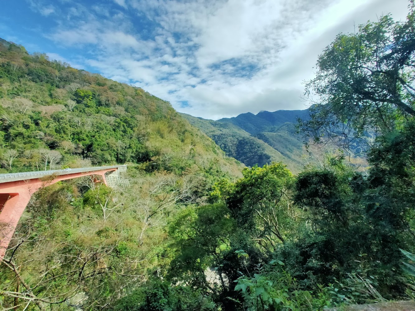 青翠山林間的紅色大橋與遠方層疊山巒