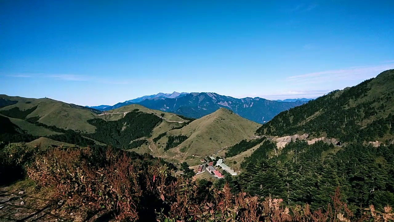 合歡山高山俯瞰，草坡起伏，山谷中有紅屋頂松雪樓建築群