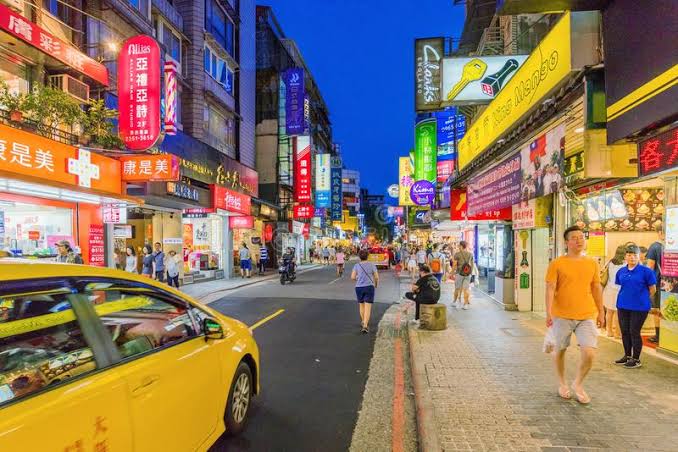 永康商圈夜晚街景，兩旁店招豐富、街上有行人與計程車。