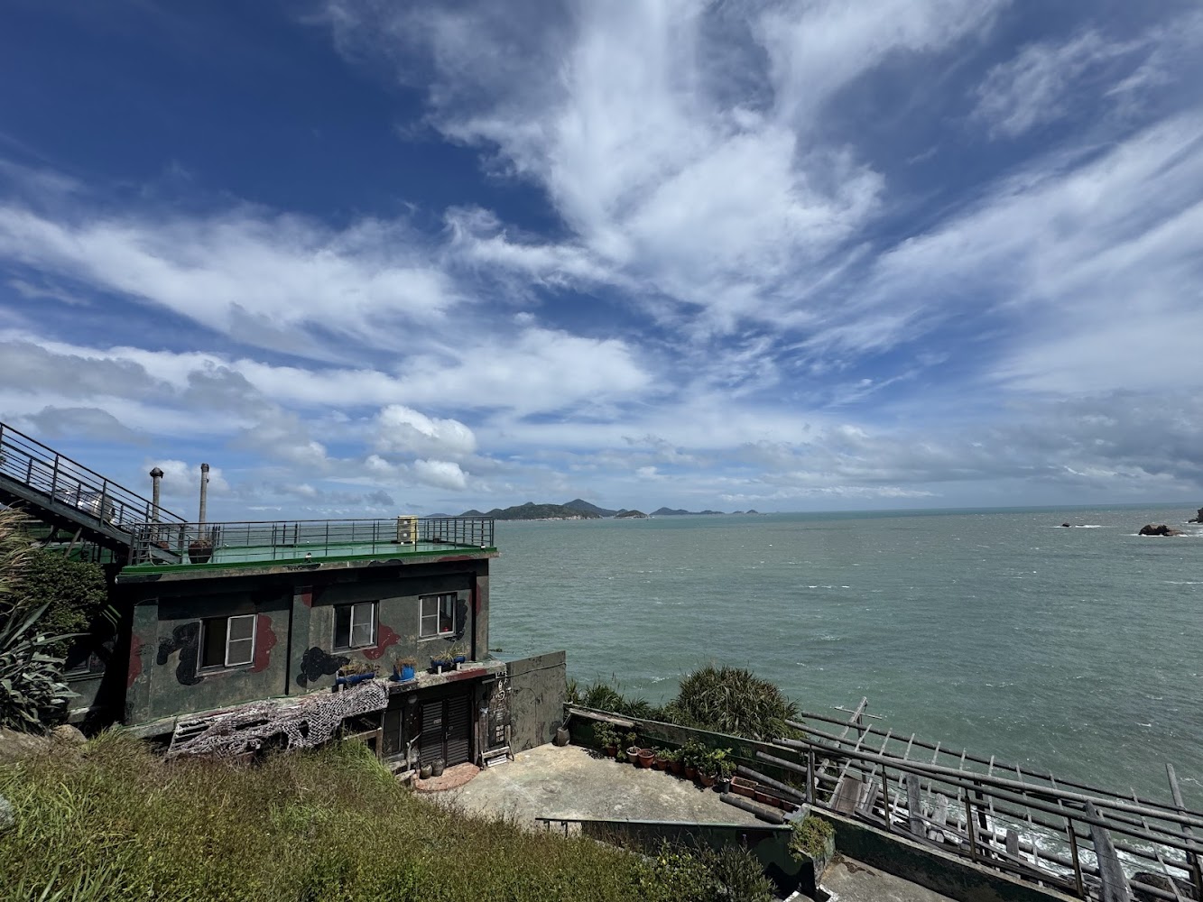 這張圖片主要展示一棟靠海的建築，前方是遼闊的大海和藍天白雲，視野開闊，氣氛寧靜自然，適合放鬆賞景。