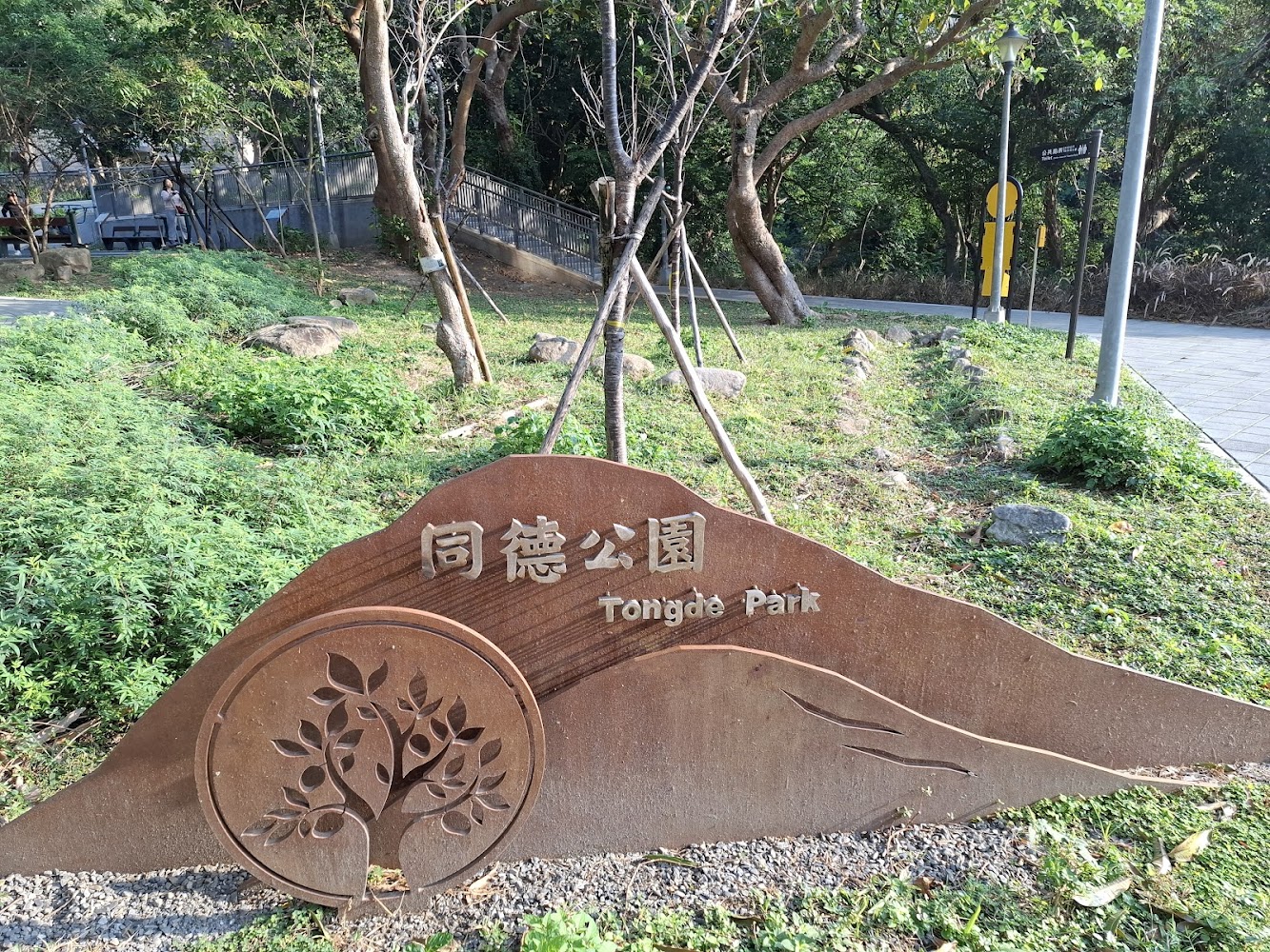 刻有同德公園與Tongde Park字樣的金屬招牌，旁邊有草地與樹木