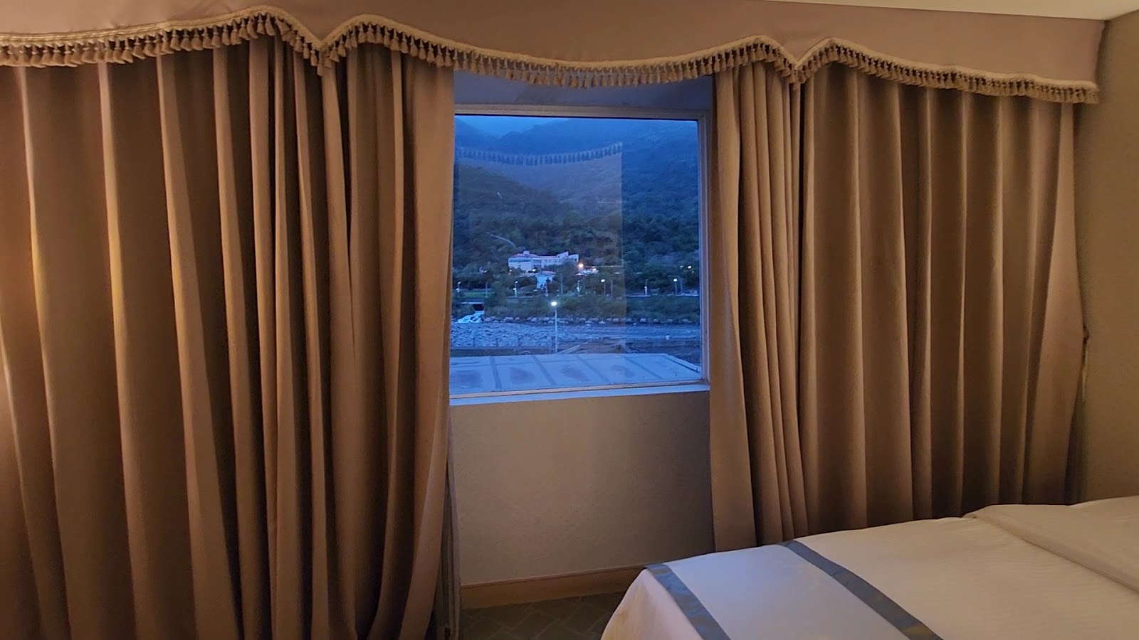富野溫泉休閒會館客房室內，棕色窗簾，窗外山林夜景，白色床鋪
