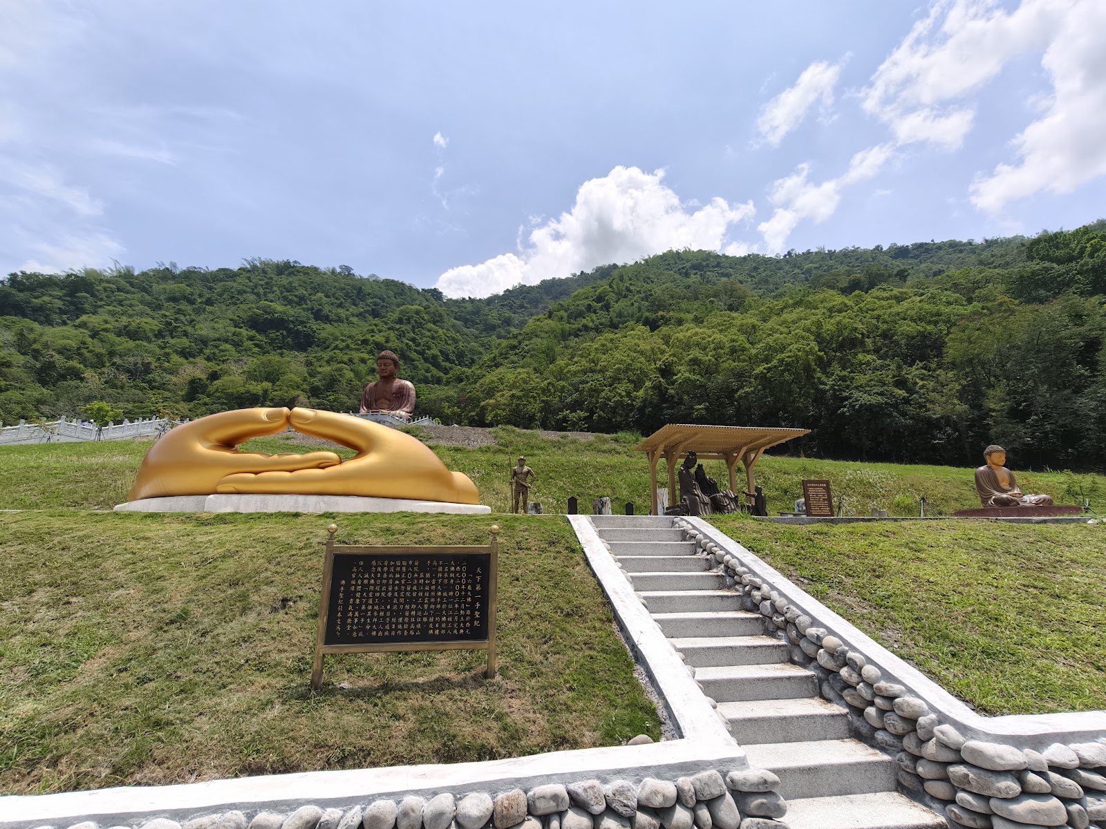 六龜大佛園區全景，金色巨型佛手雕塑居前，層層山巒為背