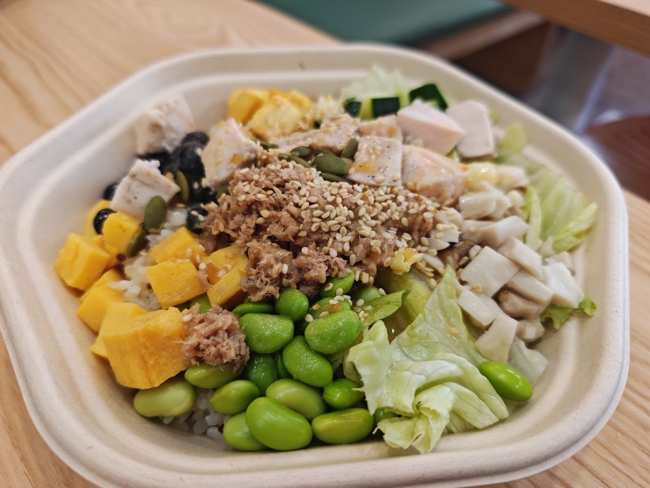 這是一份健康飯盒，主要包含毛豆、雞胸肉、玉米、南瓜、杏鮑菇、生菜、鮪魚、黑豆、黃瓜及芝麻等食材，色彩豐富且營養均衡。