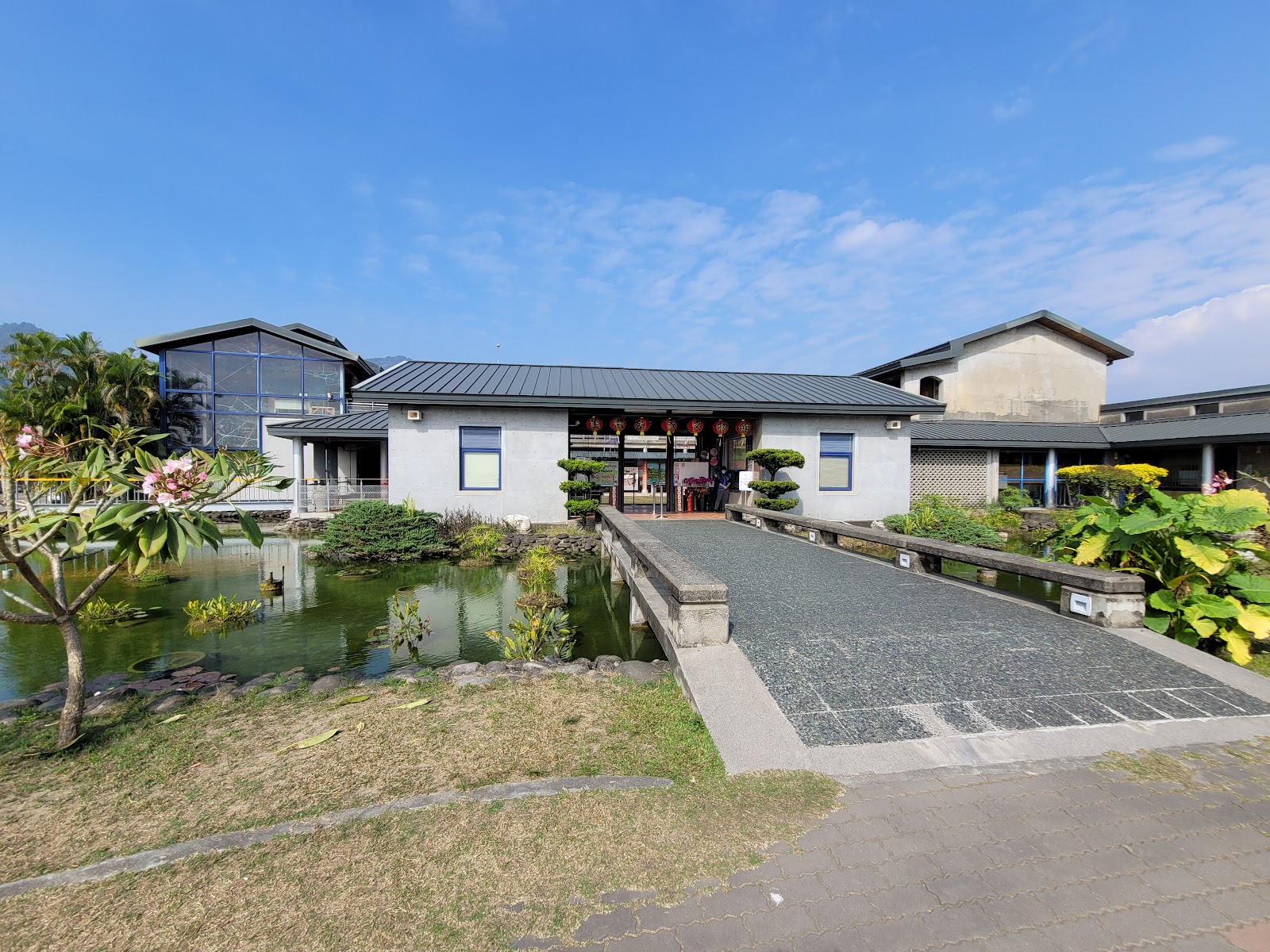 美濃客家文物館正面外觀，前有池塘造景，石板步道通往入口