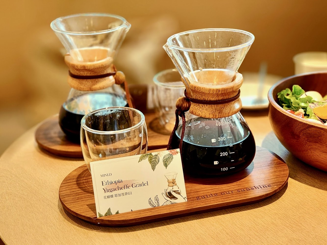 這張圖片展示了兩個手沖咖啡壺、玻璃杯和一張標示為「Ethiopia Yirgacheffe Gradel」的卡片,旁邊有新鮮沙拉,整體氛圍溫馨雅致。
