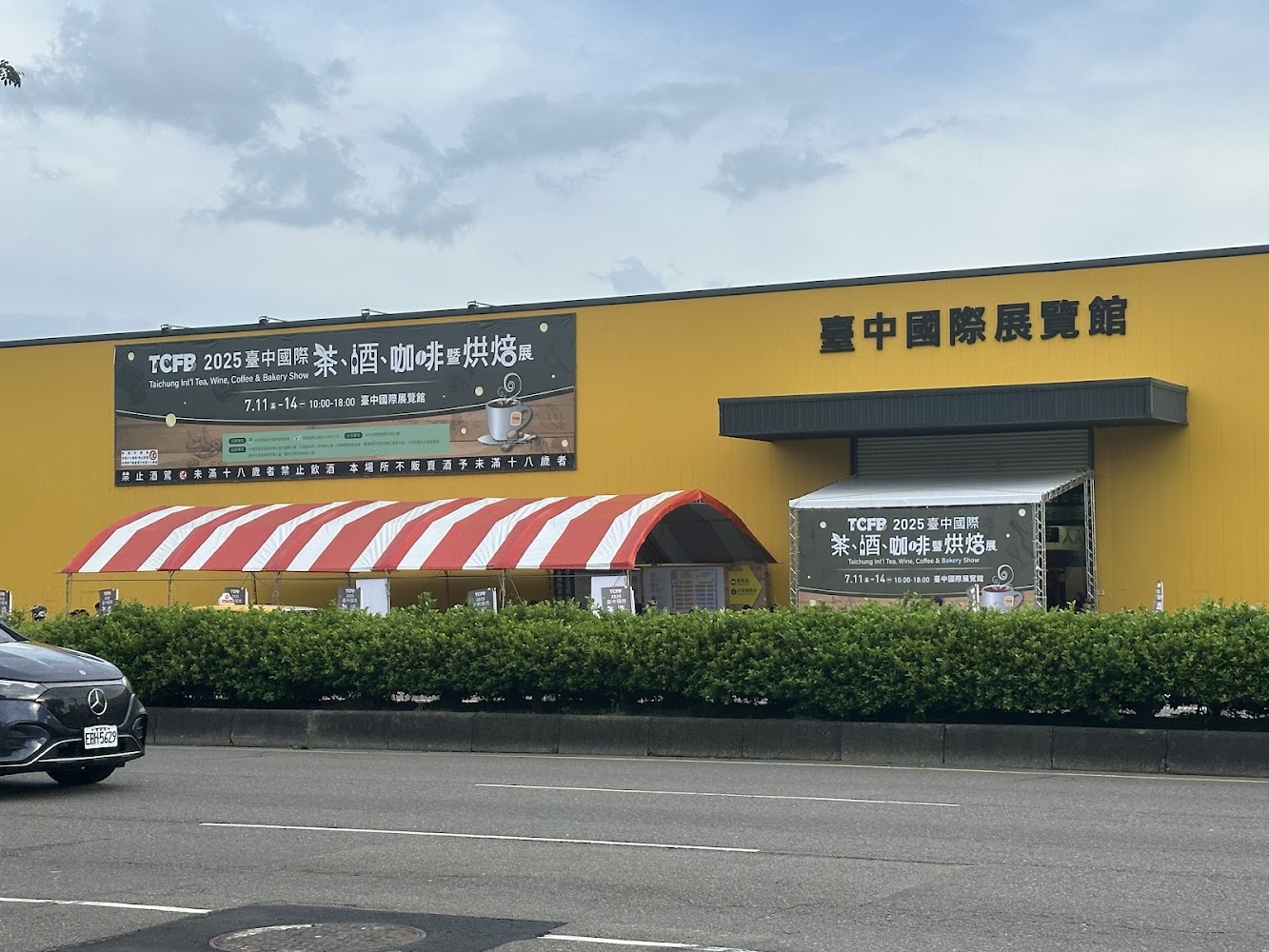臺中國際展覽館外觀與活動看板，前方有帳篷與停車車輛