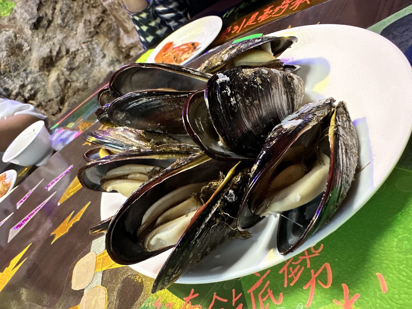 依嬤的店一盤煮熟的新鮮貽貝，旁邊可見其他海鮮與餐具