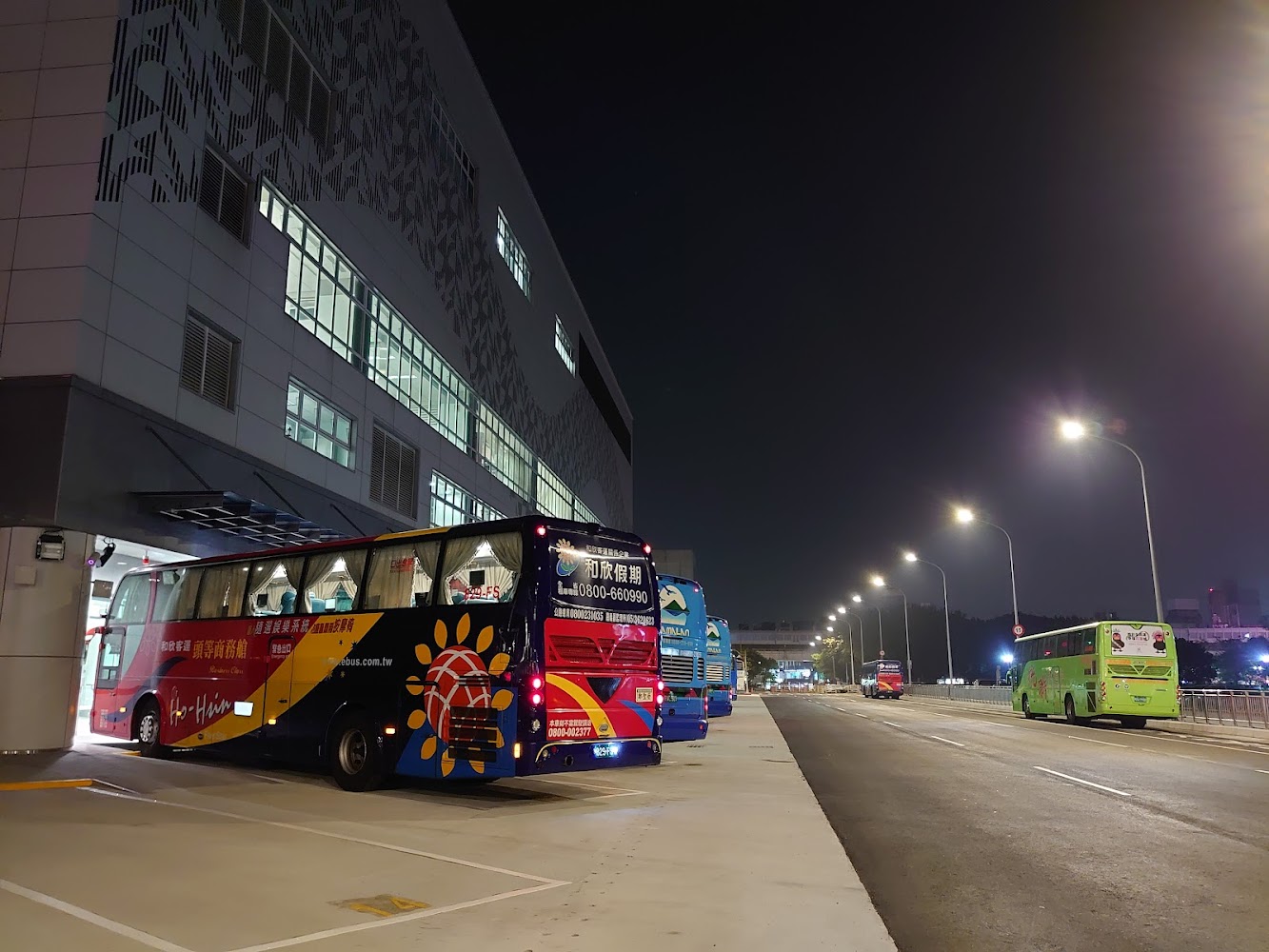 夜晚的公車轉運站，有多輛彩色大巴士停靠，周圍有明亮路燈和現代化建築