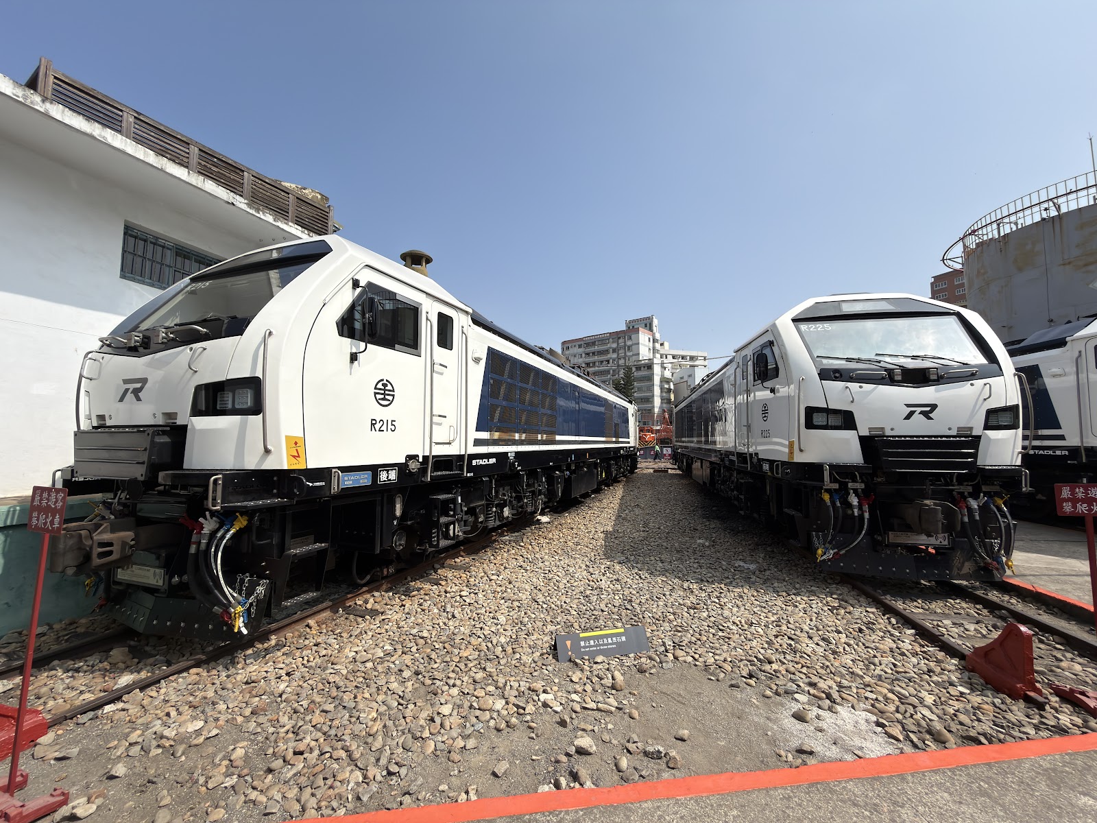 新型白色電力機車R215近景正面，台鐵標誌清晰，藍天背景，碎石道床前景