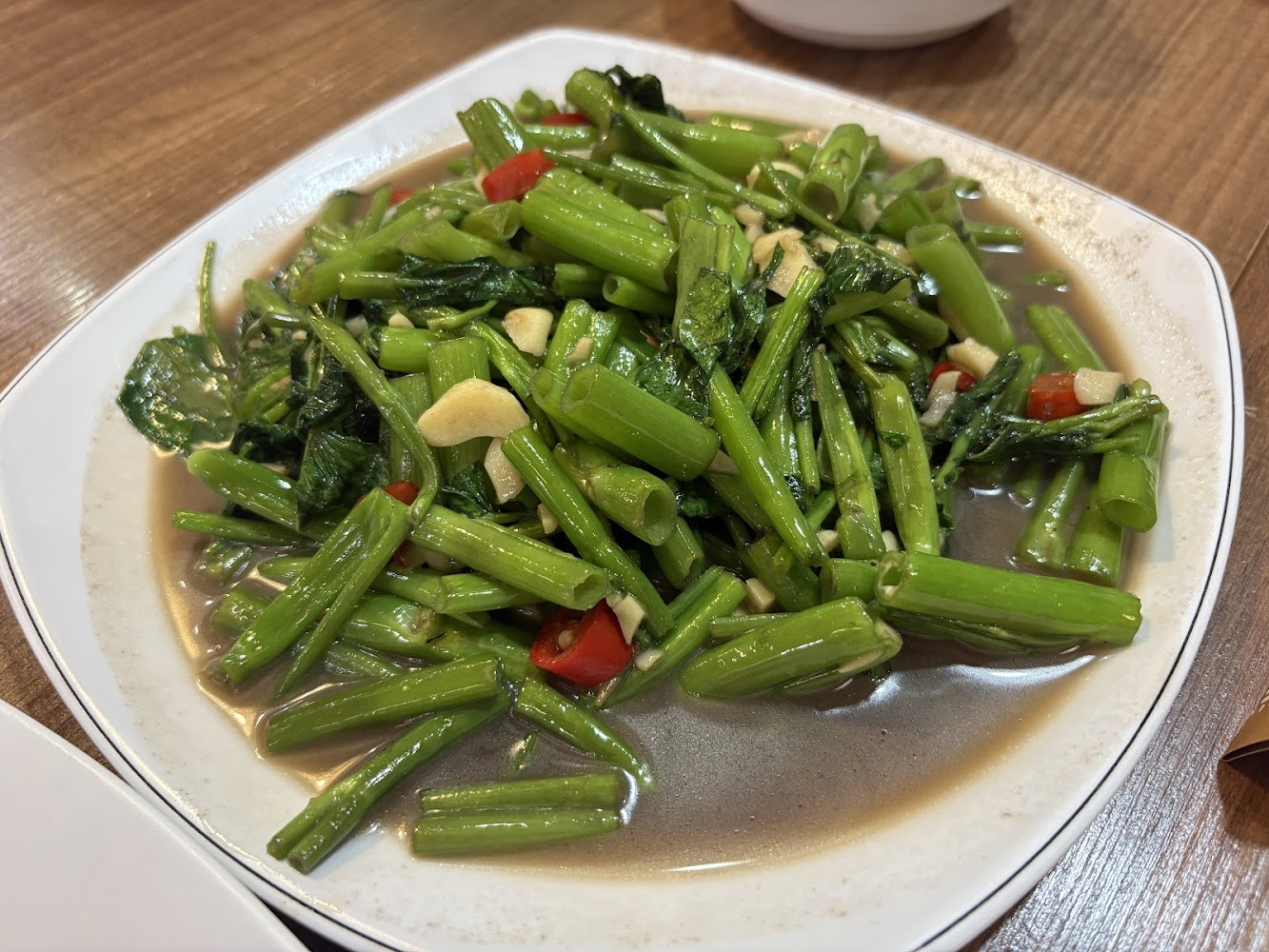 這張圖片主要是一盤炒空心菜，裡面有空心菜、蒜片與紅辣椒，呈現在白色盤子上，色澤鮮綠，看起來十分可口。