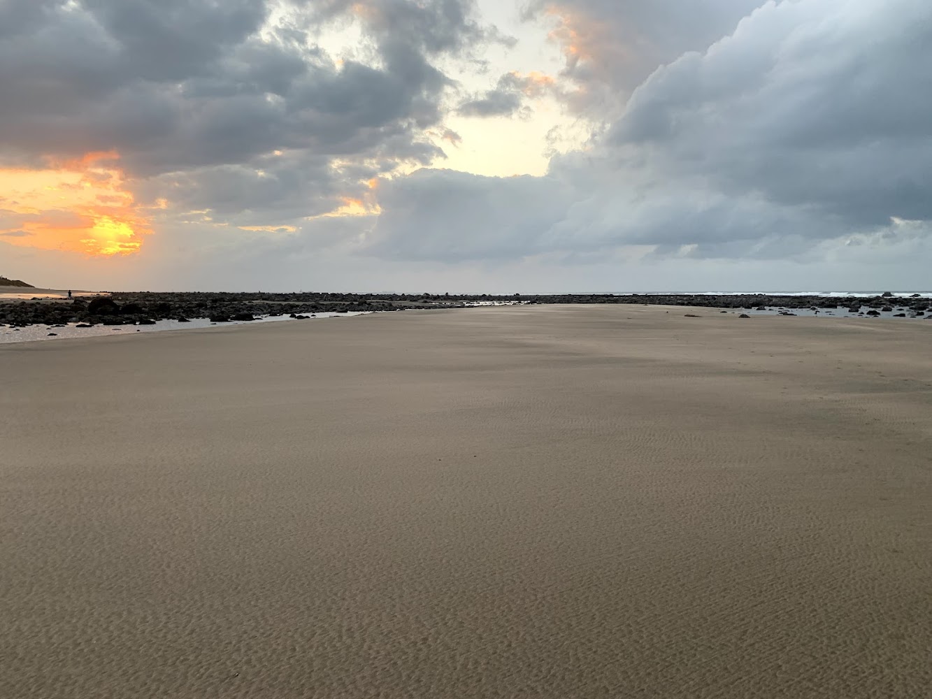 寬闊沙灘、遠處礁石海岸線與夕陽雲層的海邊景觀