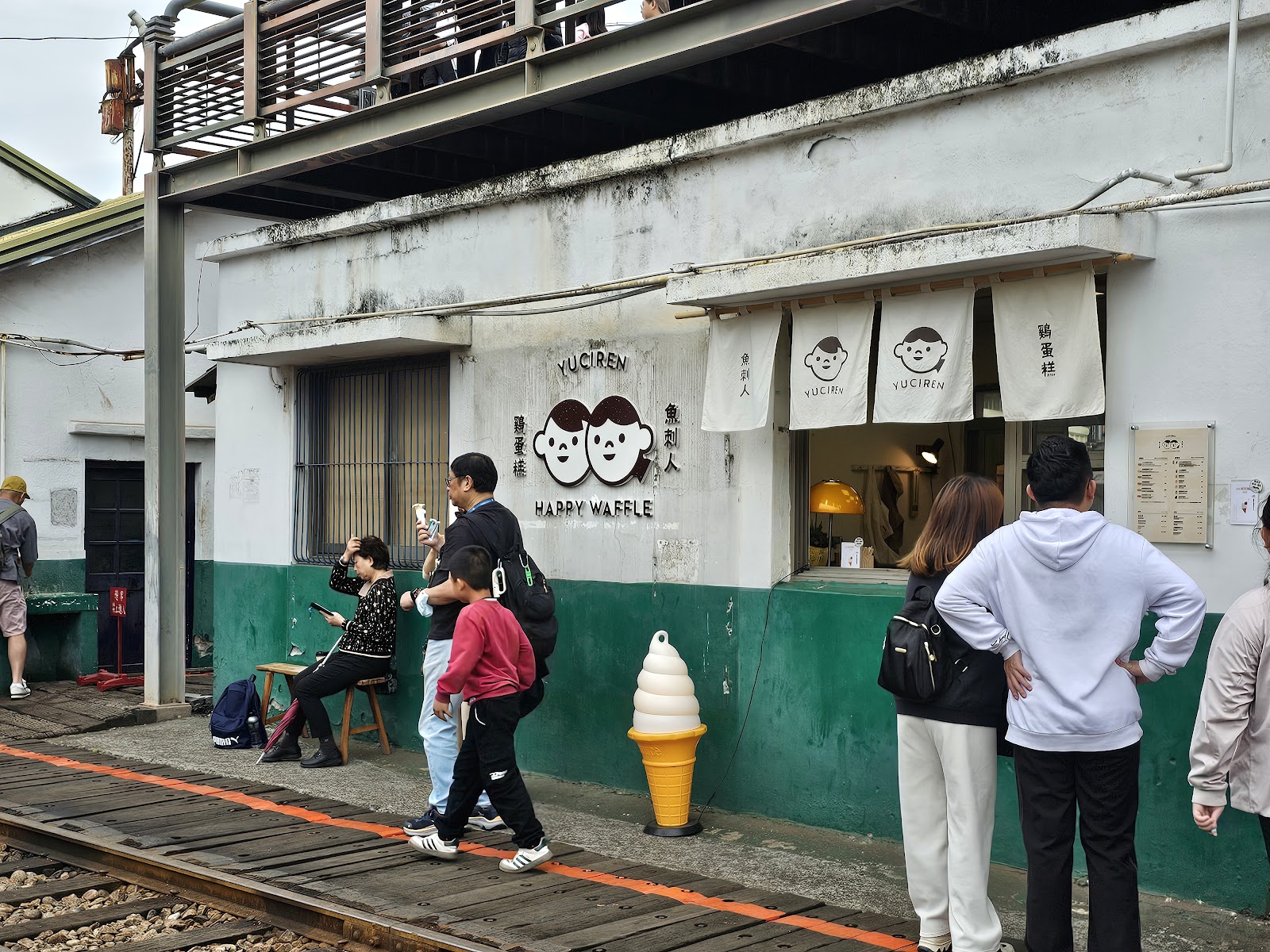 魚刺人雞蛋糕店YUCIREN HAPPY WAFFLE，白綠外牆，遊客排隊，前景冰淇淋造型裝置