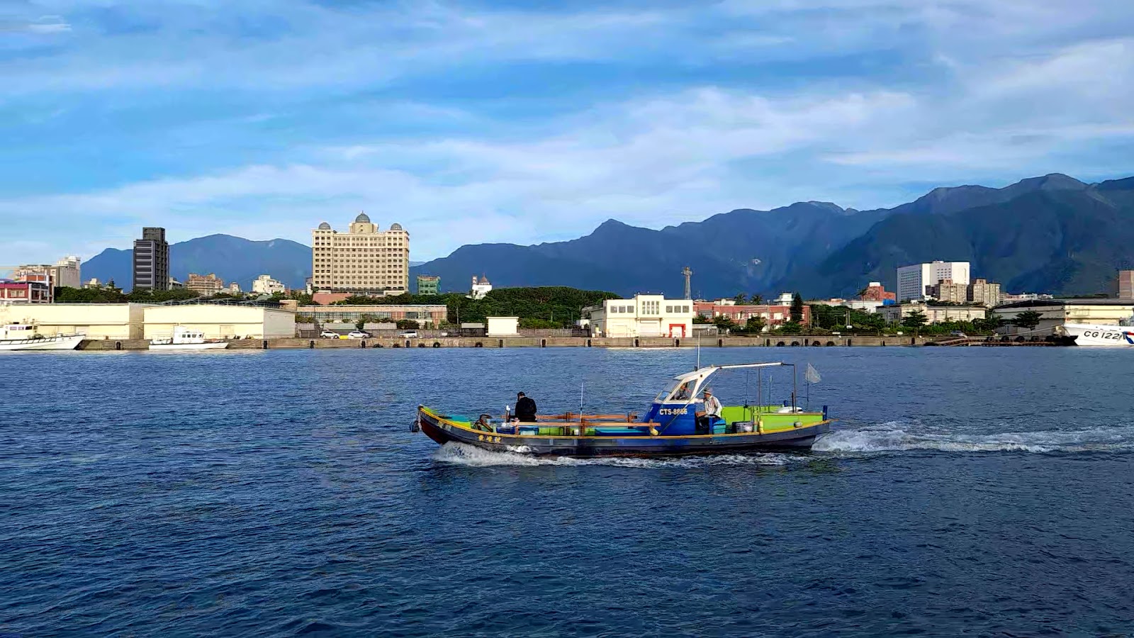 花蓮港漁船行駛海面，背景花蓮市區建築與中央山脈