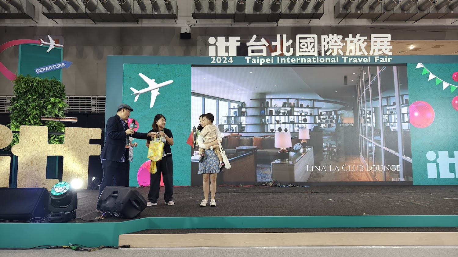 2024台北國際旅展舞台現場有三人台上互動,背景帶有飛機與出發意象