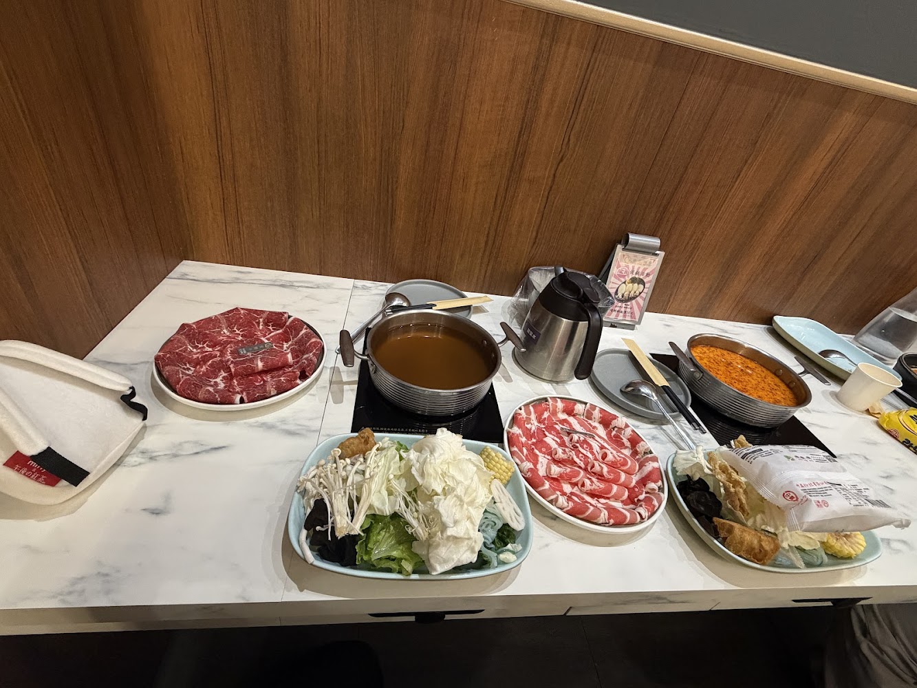 火鍋餐桌上有兩鍋湯底、蔬菜、牛肉與豬肉片。