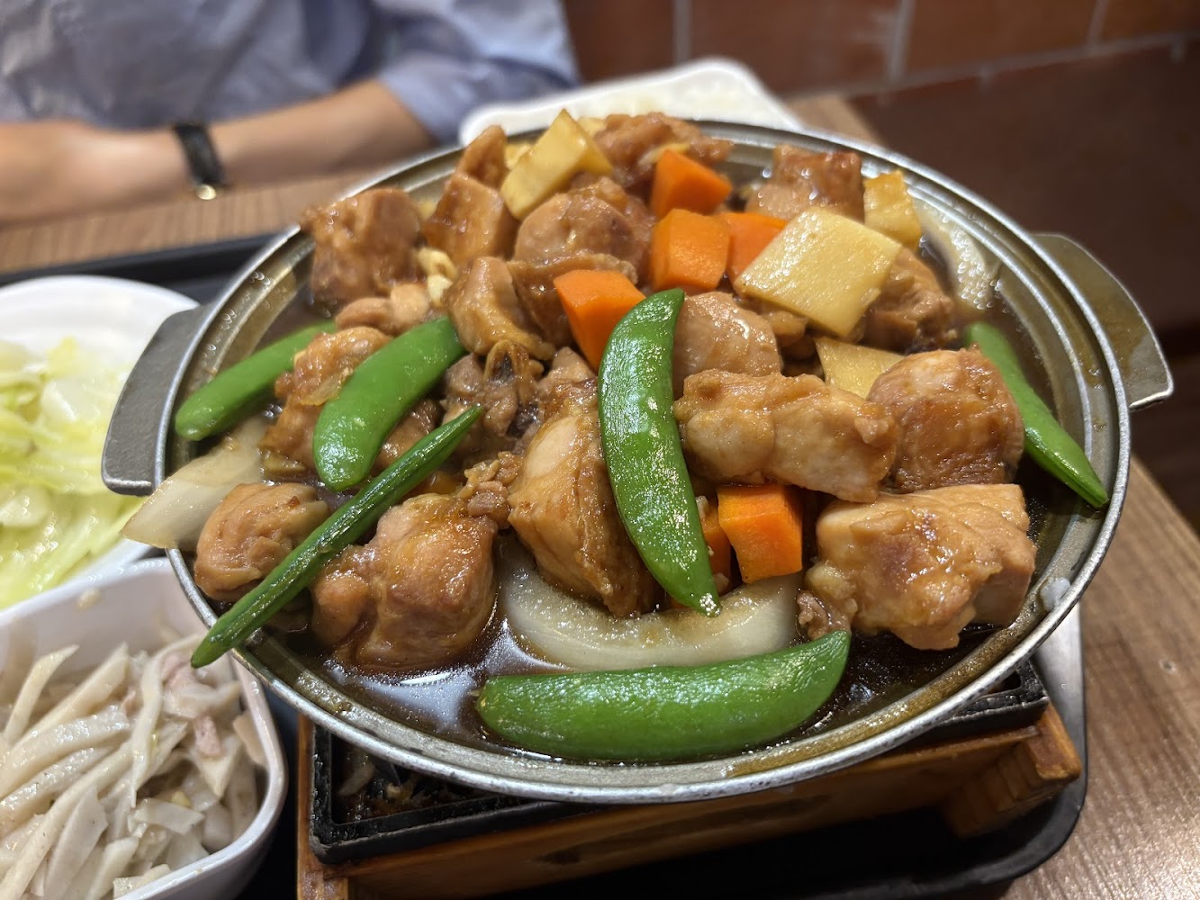 這張圖片主要是一鍋豐富的燉雞料理，裡面有雞肉塊、紅蘿蔔、四季豆、竹筍和洋蔥，色澤鮮豔誘人，旁邊還有配菜和白飯，是一道中式熱食。