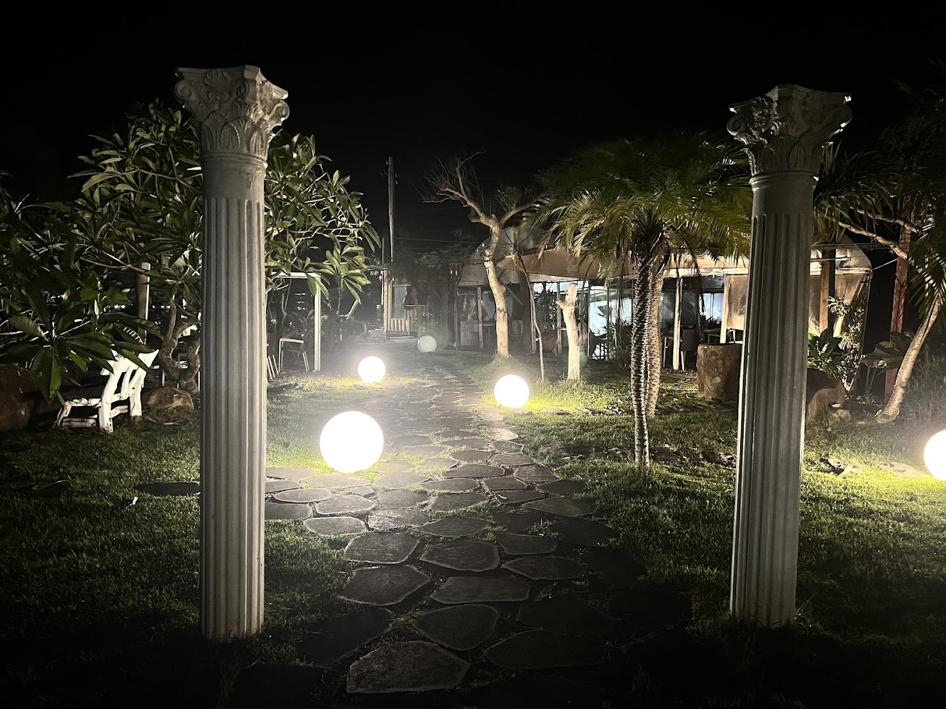 夜晚庭院，有希臘風格柱子、石頭步道與發亮的圓形燈飾