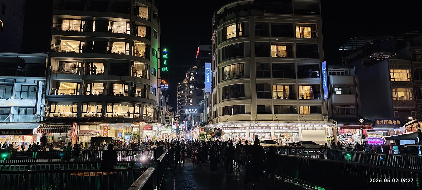 伊達邵夜間廣場全景，兩側旅館大樓燈火輝煌，人潮聚集