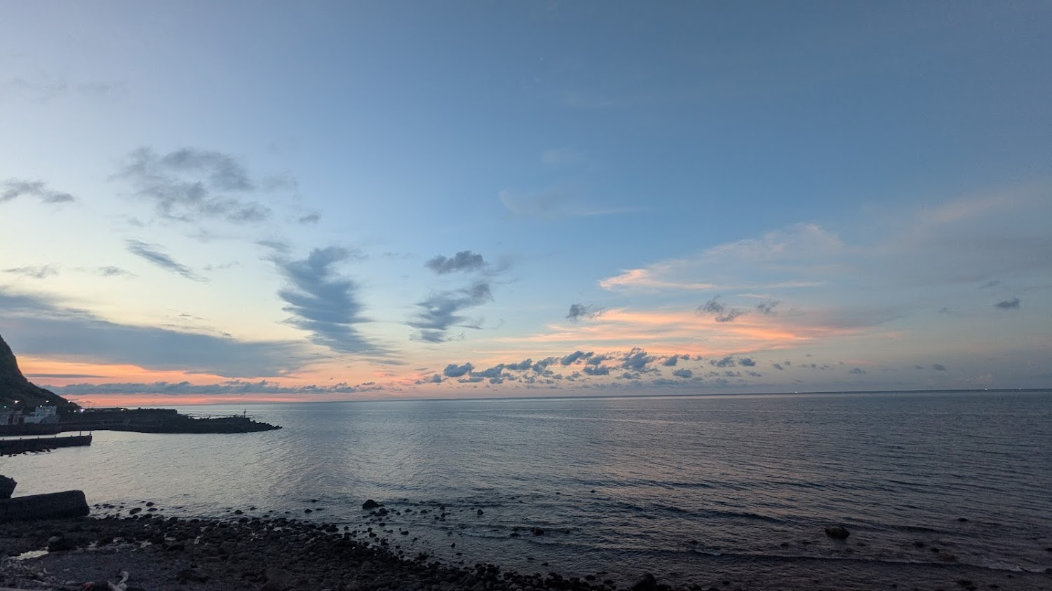 夕陽時分的海邊景色，有彩霞雲朵、寧靜海面與港灣