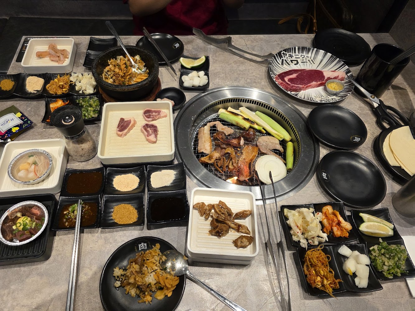 桌上有各種生肉、蔬菜、石鍋拌飯、泡菜和多種醬料的韓式燒烤餐