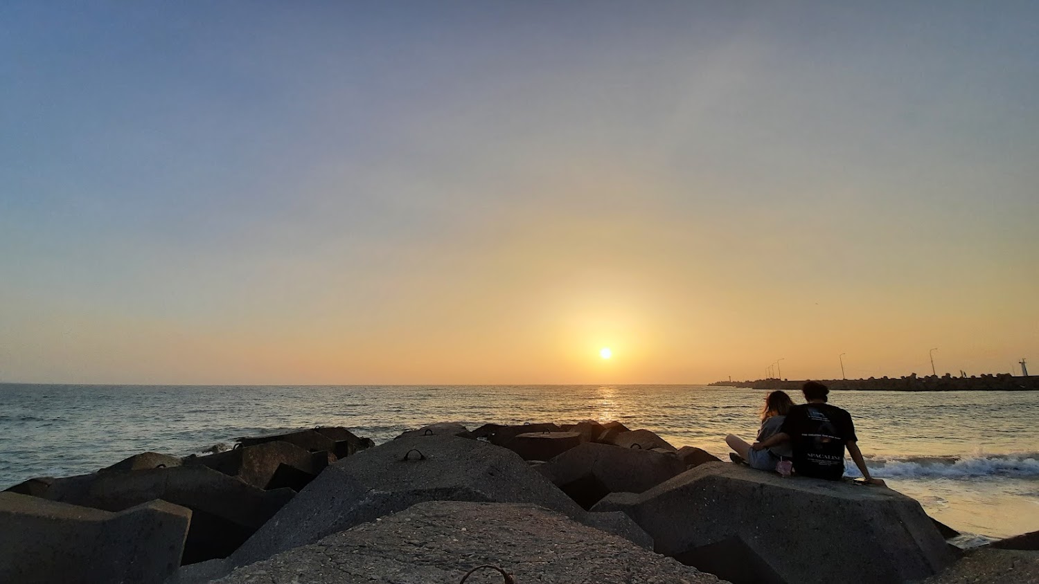 夕陽下情侶坐在防波塊上的浪漫景色