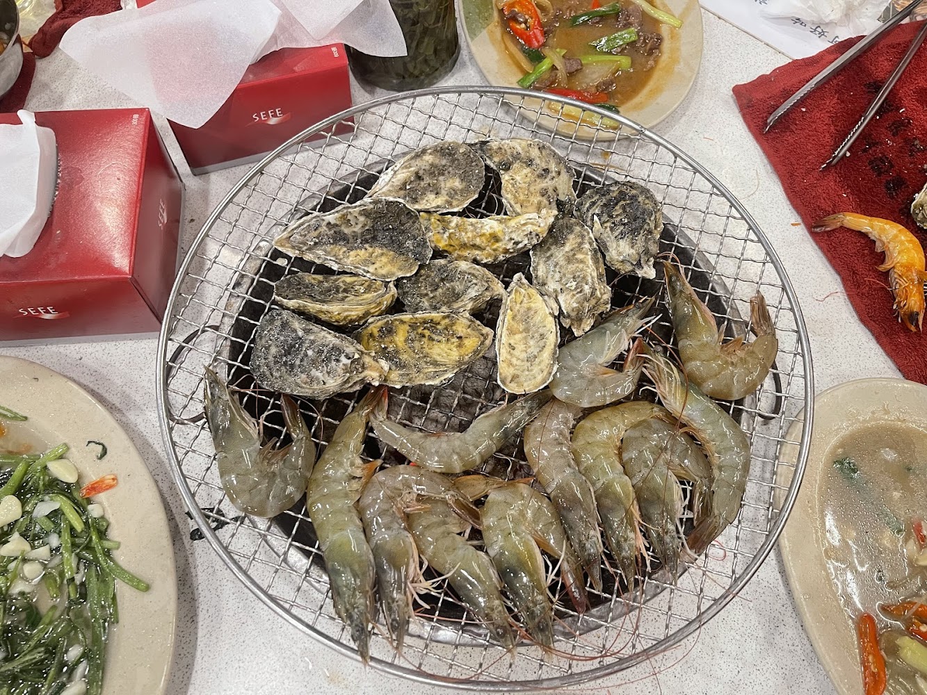 烤網上烤著生蠔與蝦子旁有炒青菜