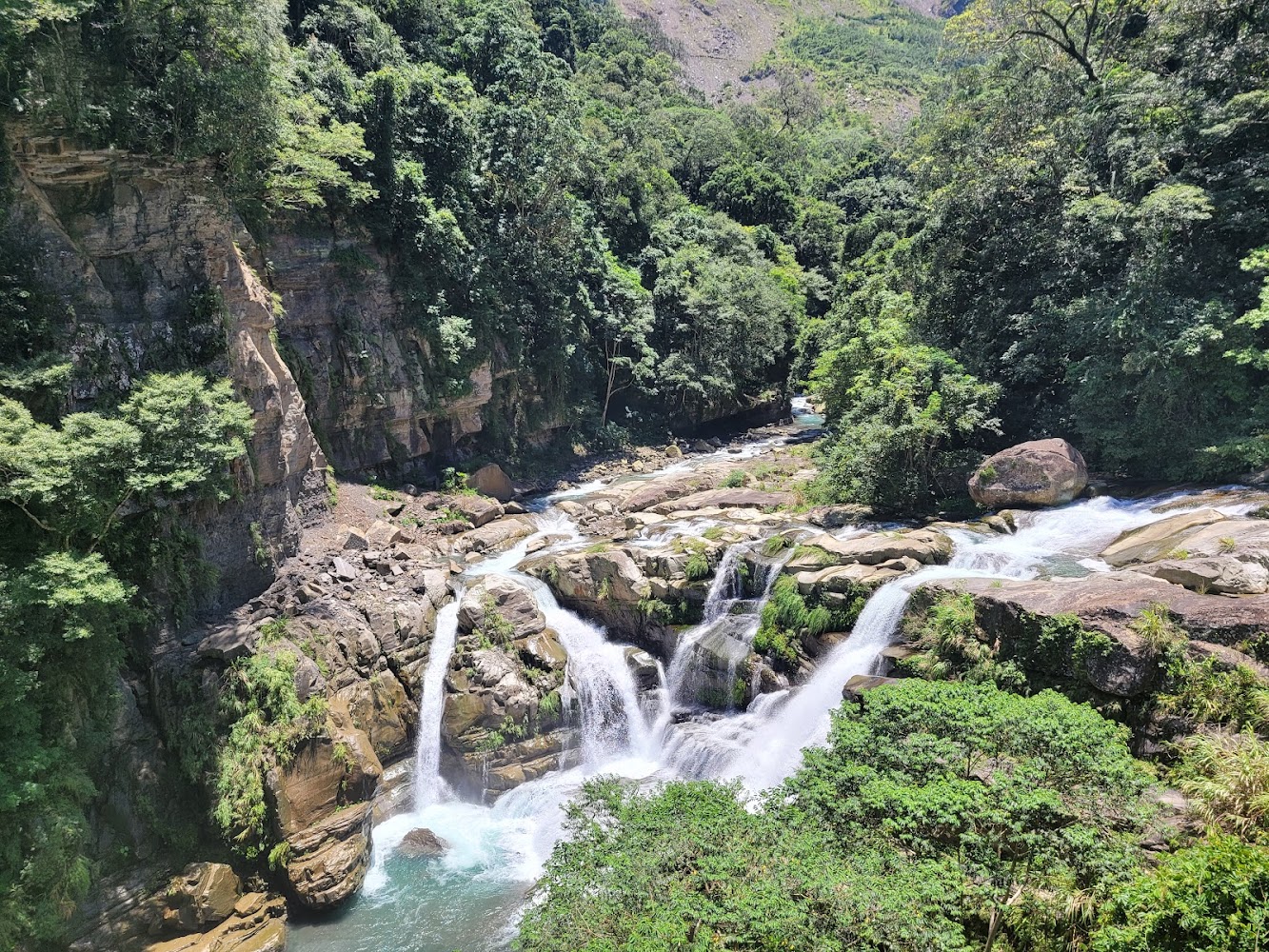 山間瀑布水流分成多股墜落,四周被樹林和岩壁環繞。