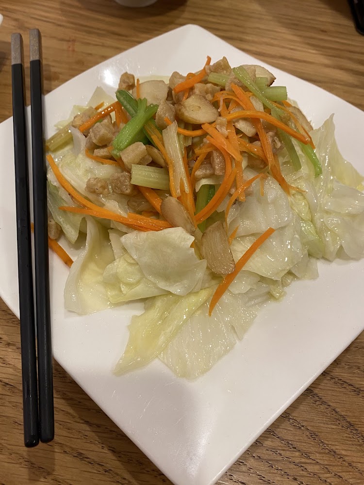 這張圖片主要是炒高麗菜，裡面有高麗菜、紅蘿蔔絲、蒜片與蔥段，還有一些切丁的配料，看起來炒得很清爽健康。旁邊放著一雙黑色筷子。