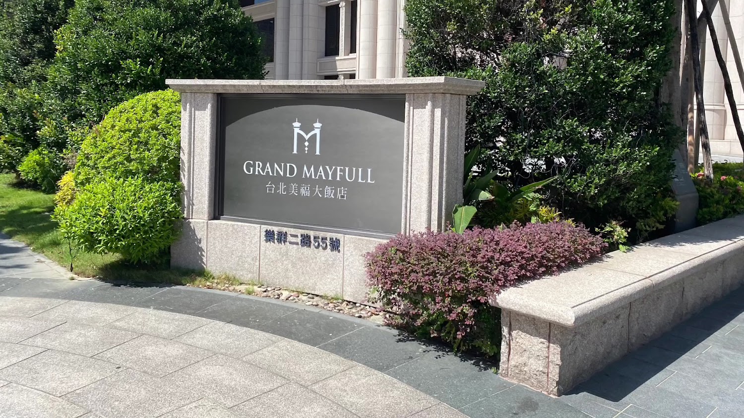 飯店門口標示牌，寫有台北美福大飯店，周圍有綠色植栽與石造長椅。