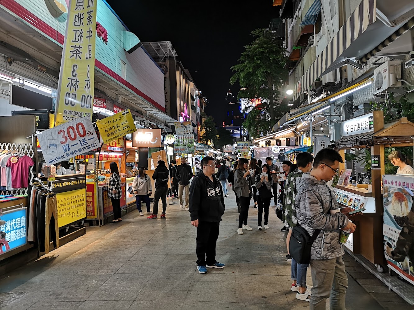 熱鬧街道兩旁有小吃攤與店家，許多人排隊逛街。