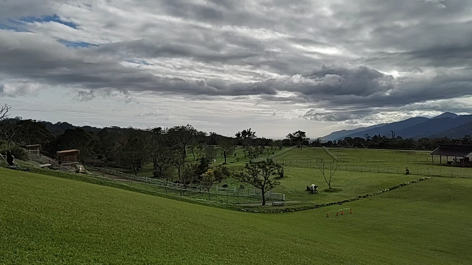 初鹿牧場廣闊草地全景鳥瞰，白色圍欄環繞，遠方山脈連綿