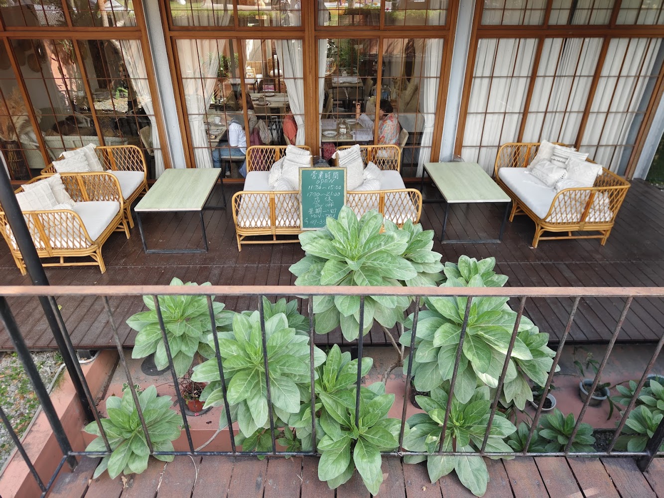 戶外休息區有竹編沙發、白色靠墊和綠色桌子，前景有植物