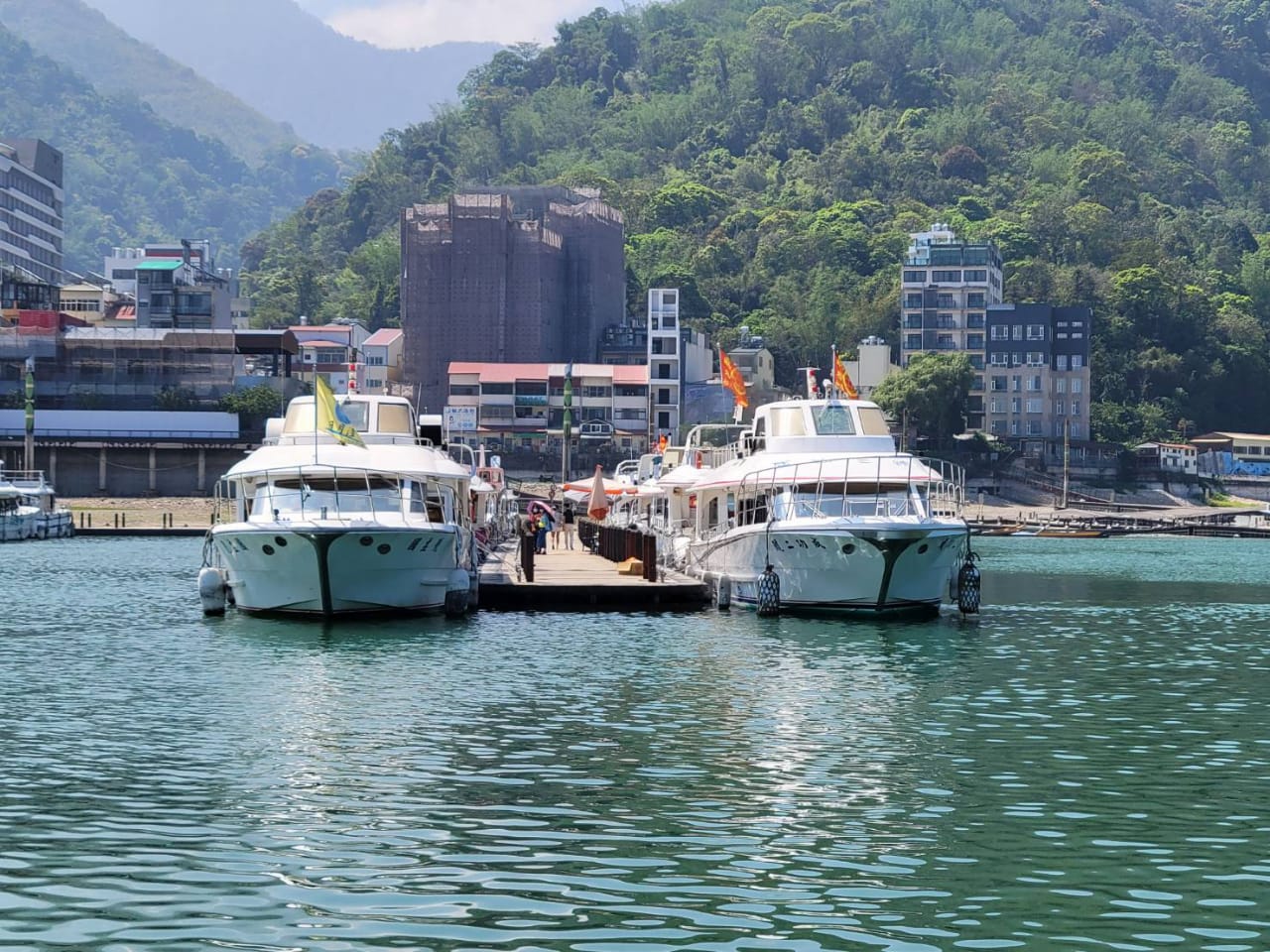兩艘停靠在碼頭的遊艇與山林建築景色