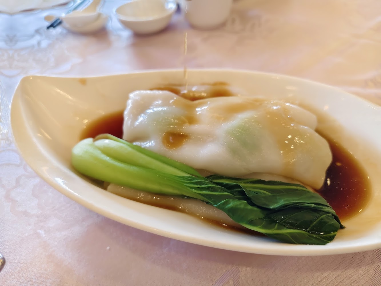 中式點心腸粉,放在白色橢圓碟中,旁邊有一根青江菜,淋上醬汁