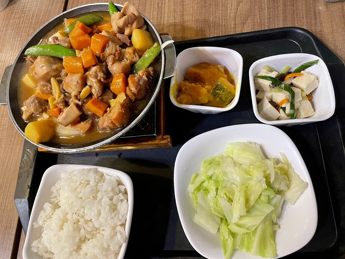 這張圖片是一套台式家常套餐，有燉雞肉、白飯、燙青菜，還有兩道配菜，包括南瓜和豆干炒蔬菜，整體看起來營養均衡豐富。