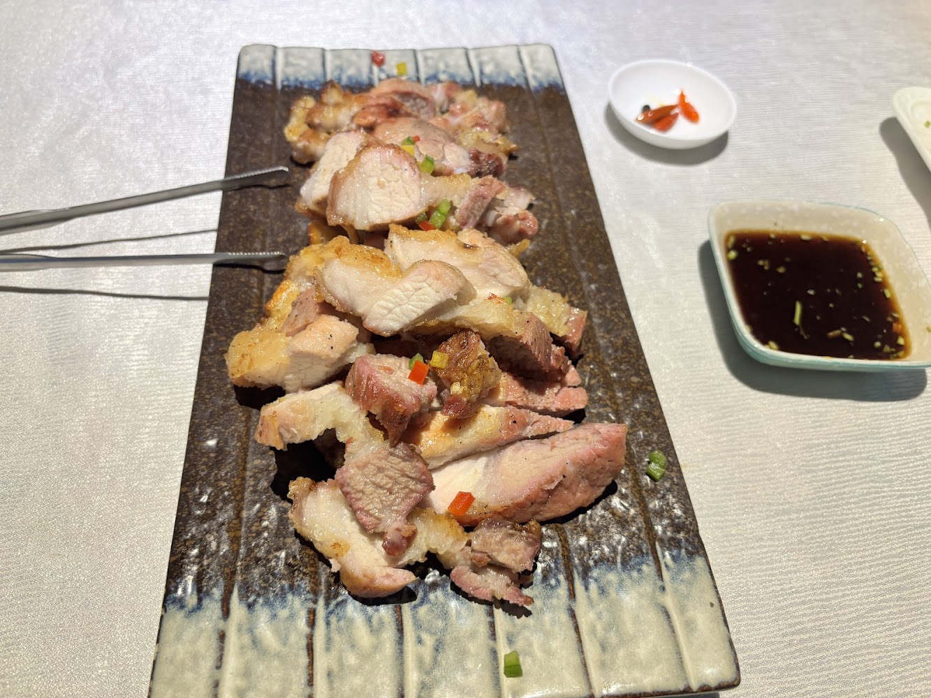 切片烤豬肉，肉質鮮嫩多汁，旁邊附醬油與辣椒