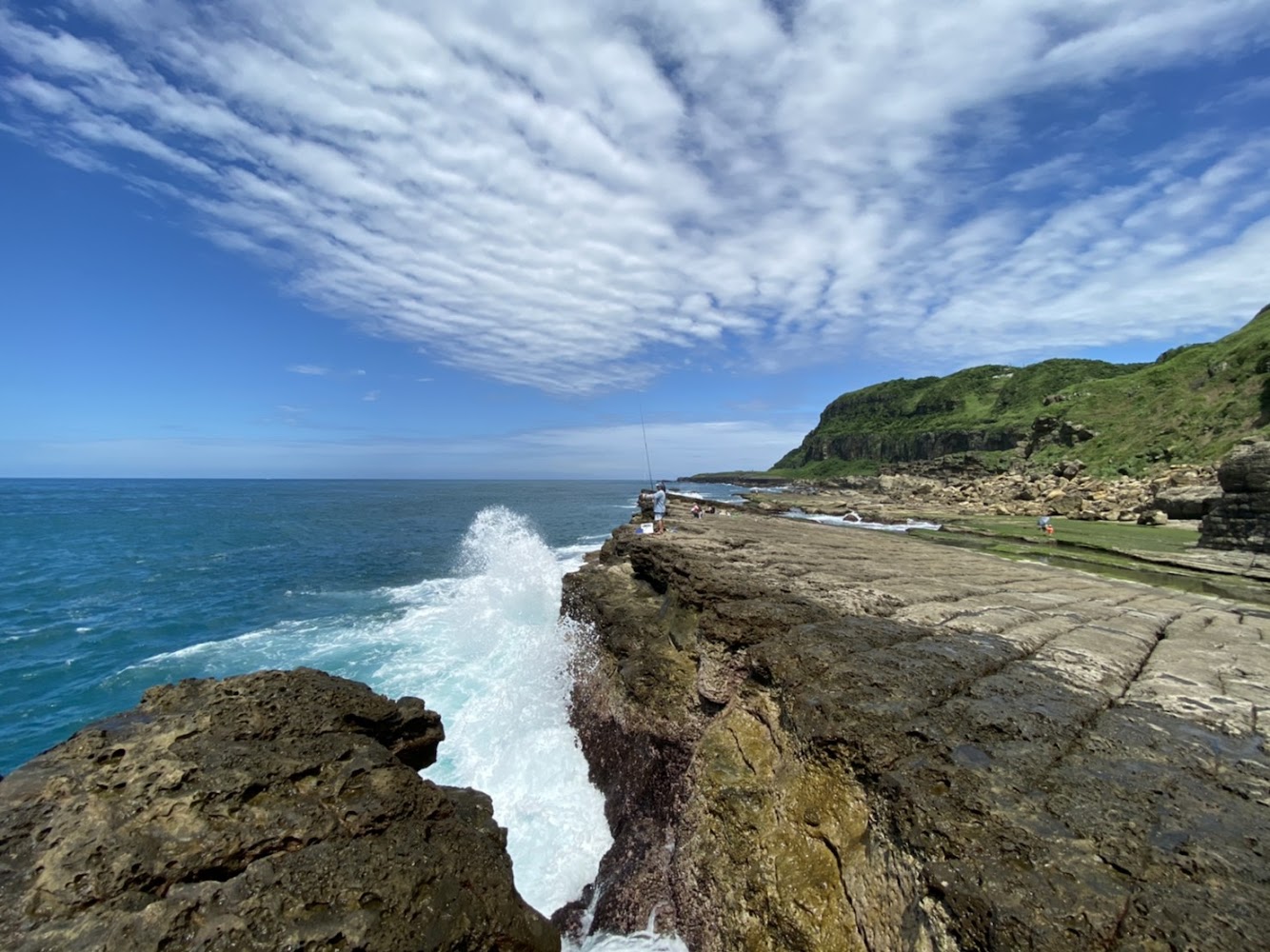 壯闊海岸線與岩岸浪花，遠方有山丘與遊人