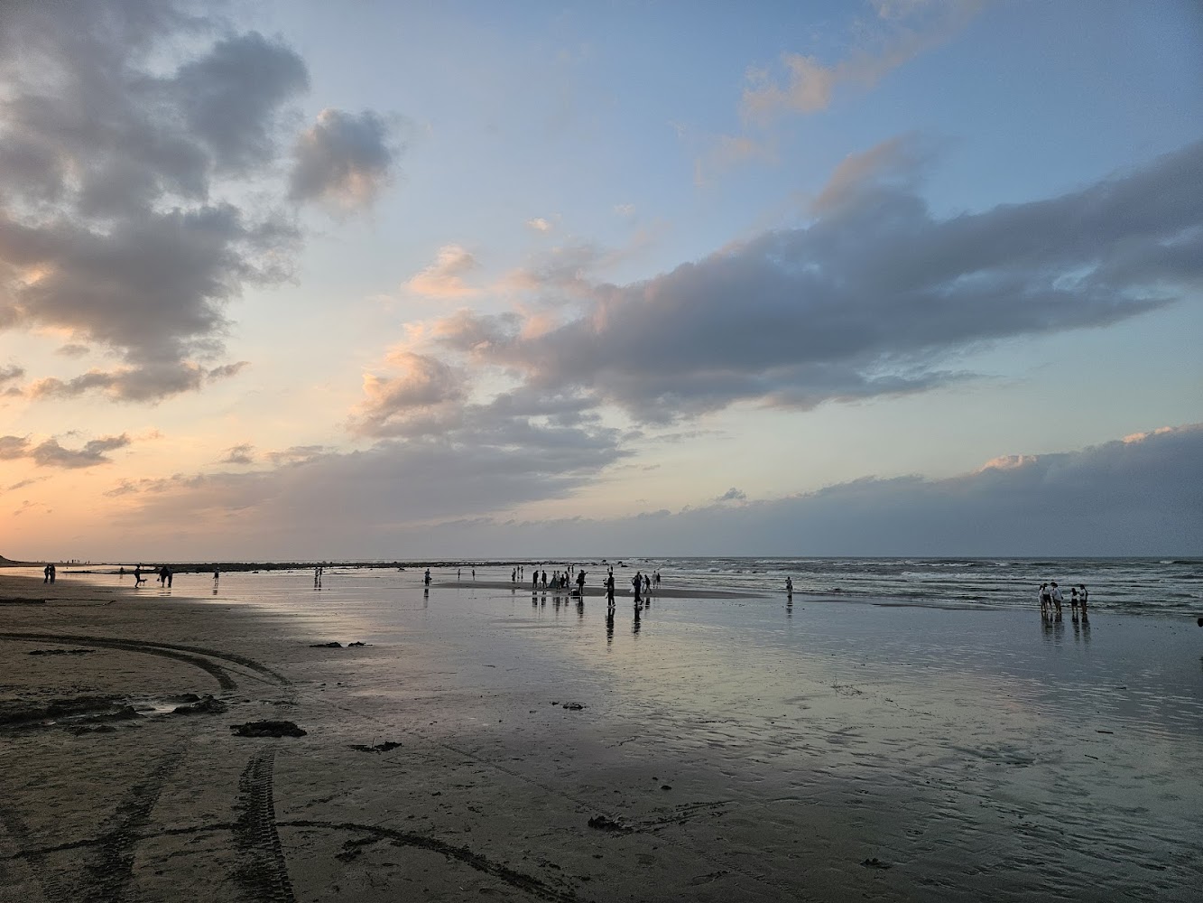 夕陽西下天空雲彩繽紛，沙灘上有人散步的海灘風景