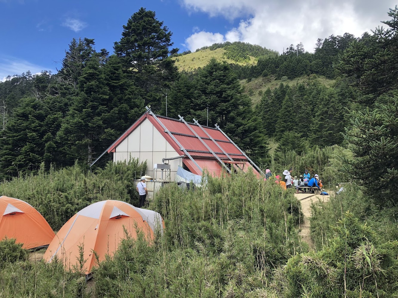森林中的山屋旁有橘色帳棚與登山者