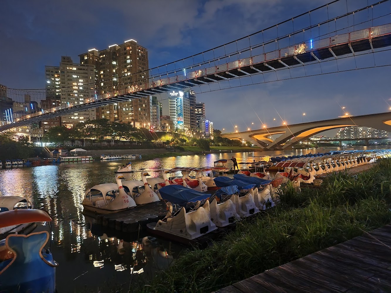 夜晚河邊整齊排列的天鵝船，城市燈光倒映在河面上