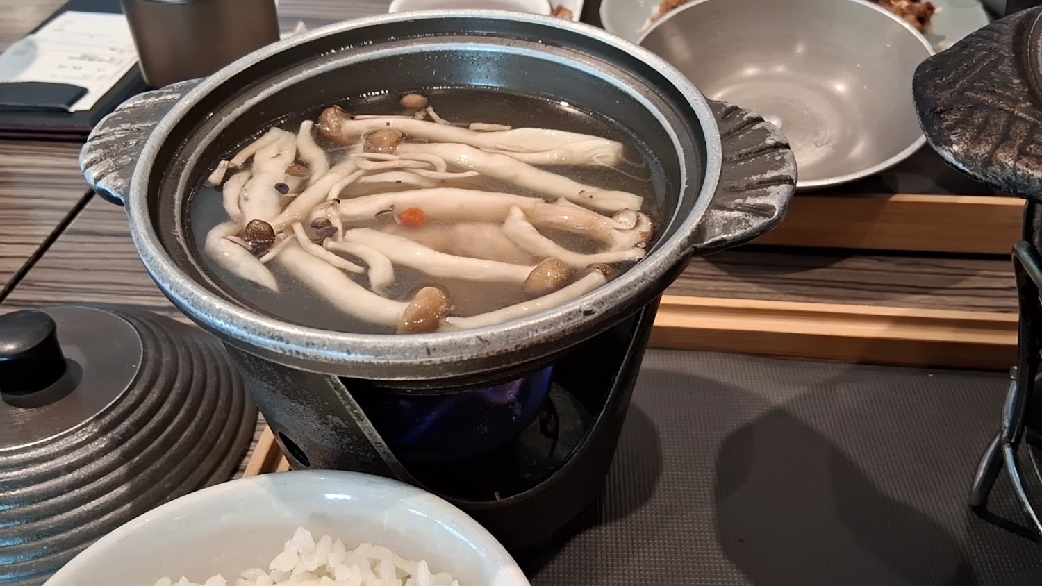 一鍋火鍋，鍋中有各種菇類和湯底，旁邊有白飯