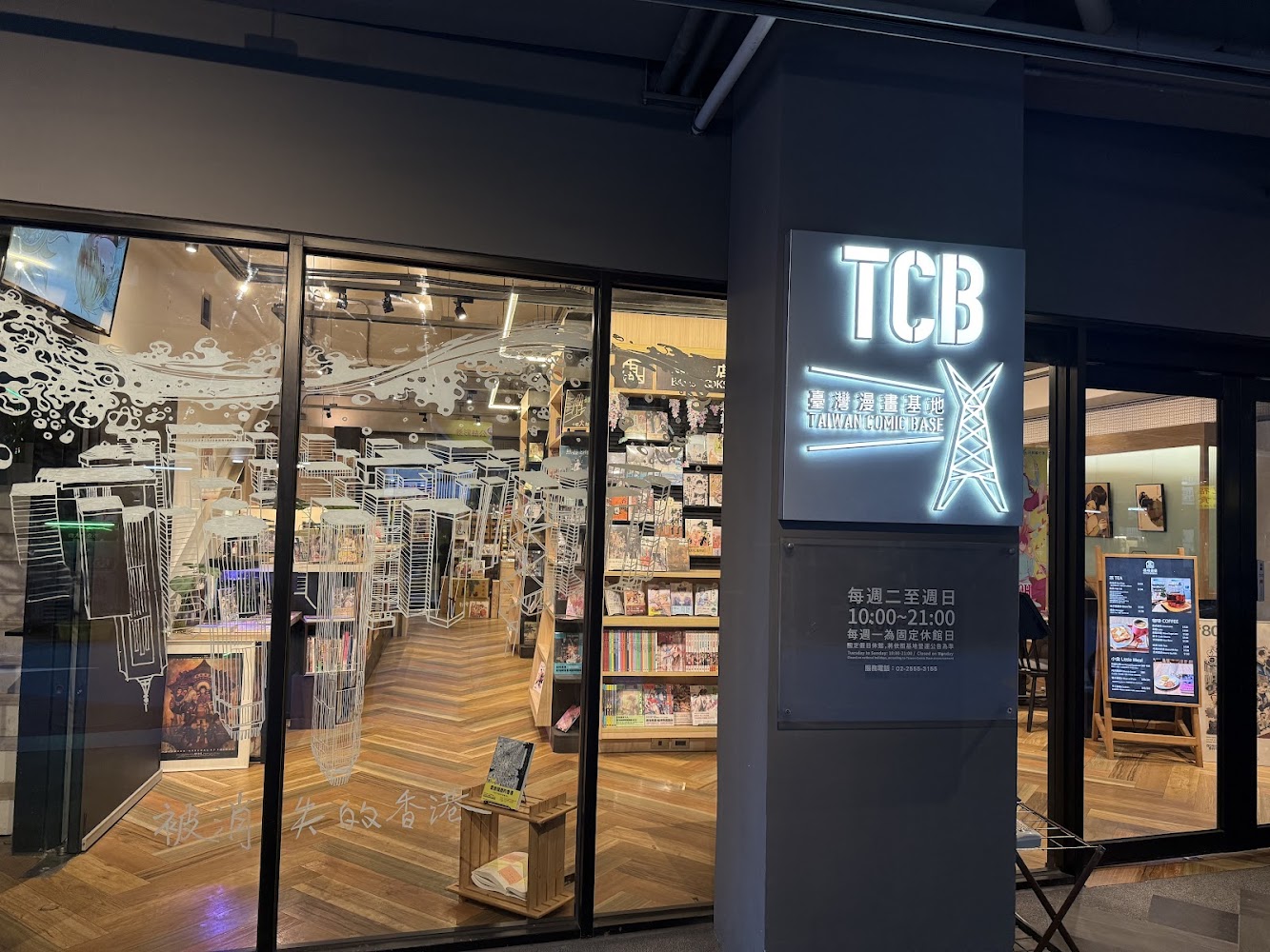 這張圖片主要展示了一家名為台灣漫畫基地(TCB)的店面,店內可見大量漫畫書籍和展架,外牆有明亮的TCB招牌,玻璃上有白色插畫裝飾,沒有明顯浮水印。