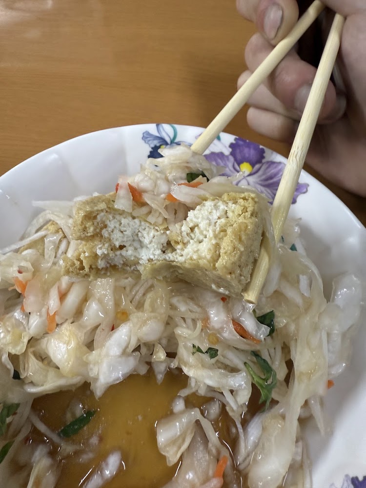 筷子夾起半塊臭豆腐，盤中有泡菜與醬汁